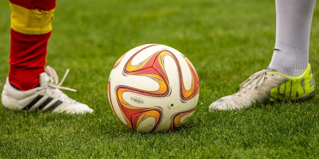 En fotboll med två olika fotbollsskor på två olika fötter.