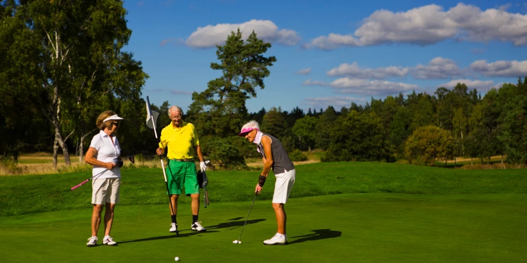 Tre äldre människor spelar golf på en golfbana.