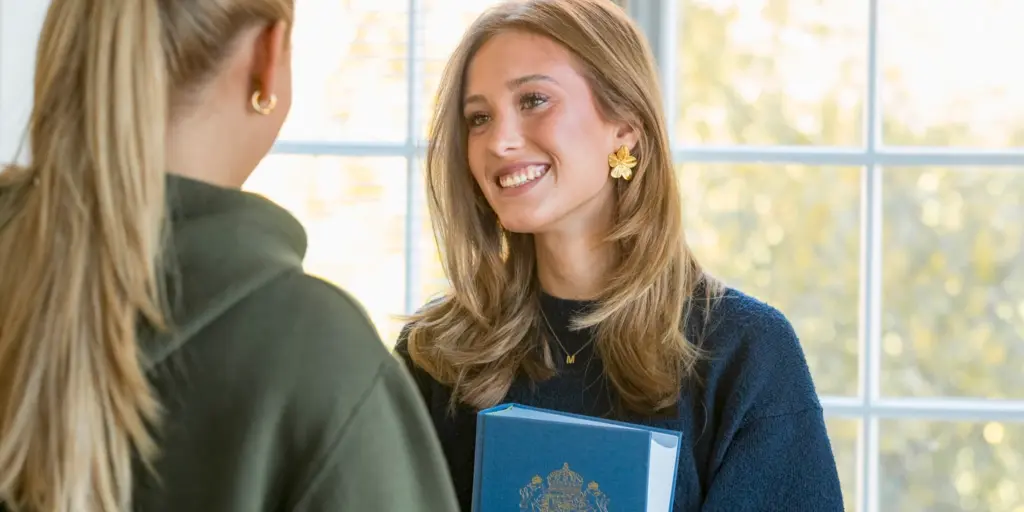 En kvinna pratar med en annan kvinna som håller i en bok