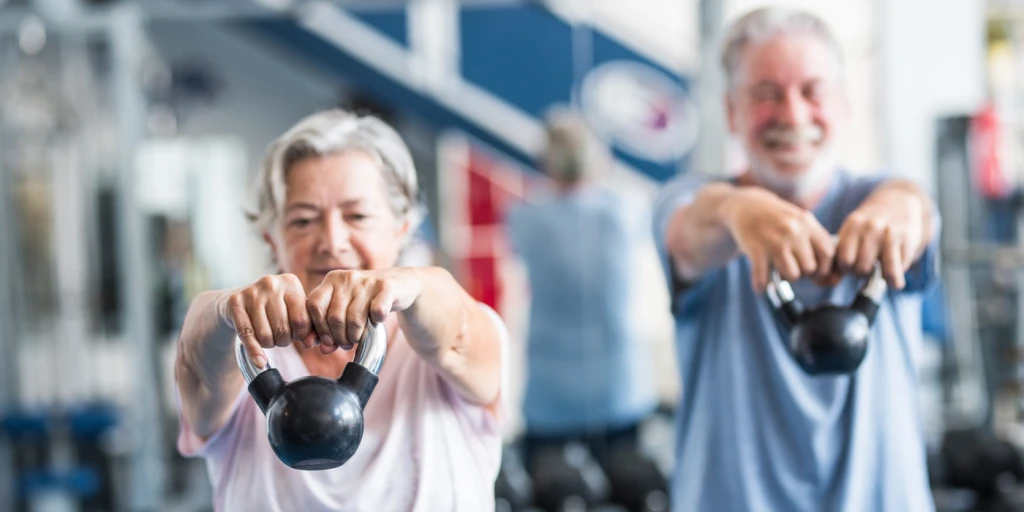 Ett äldre par tränar med kettlebells på ett gym.