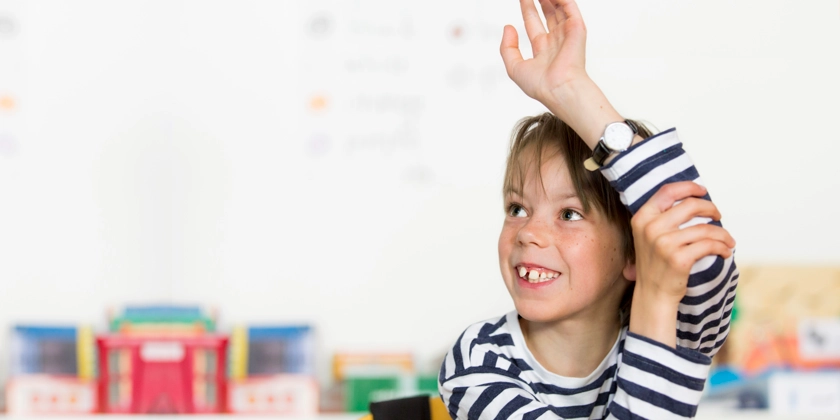 En pojke i randig tröja räcker upp handen i skolan.