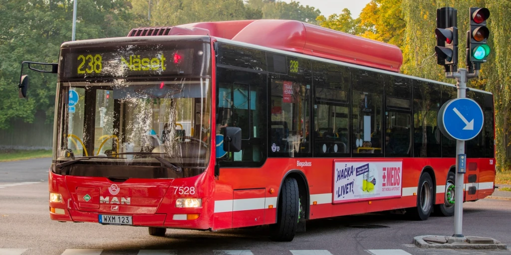 En röd buss svänger i en korsning med trafikljus.