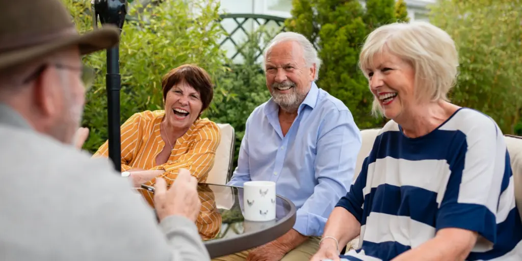 Ett skrattande seniorsällskap sitter och fikar utomhus.
