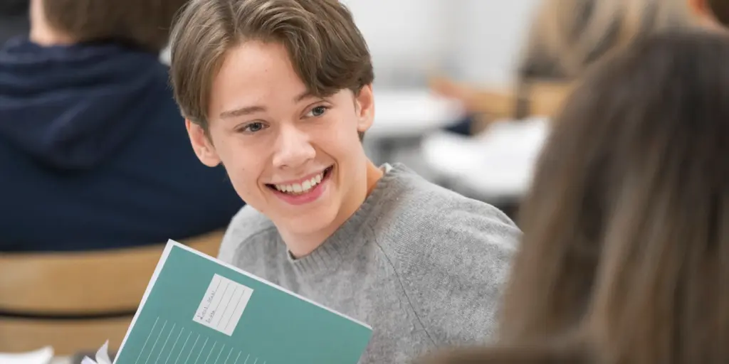 En leende ung pojke håller i ett skrivhäfte på Hersby gymnasium.