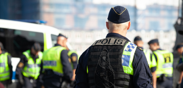 Ryggtavla på polis i förgrunden och andra poliser i västar i bakgrunden