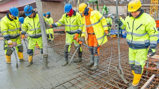 Gulklädda arbetare som häller betong genom armeringsjärn.