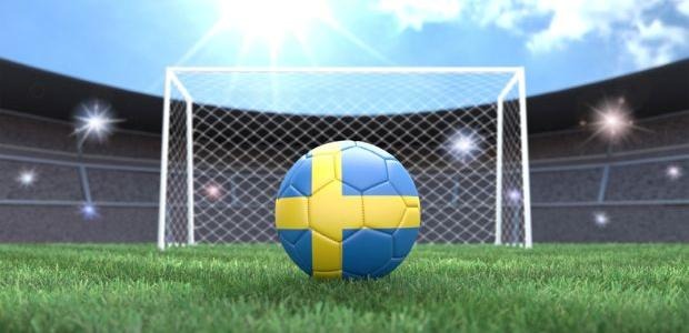 En fotboll med svenska flaggans färger på en fotbollsarena, ett fotbollsmål framför.