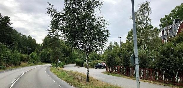Asfalterad större väg med ett hus och träd vid sidan.