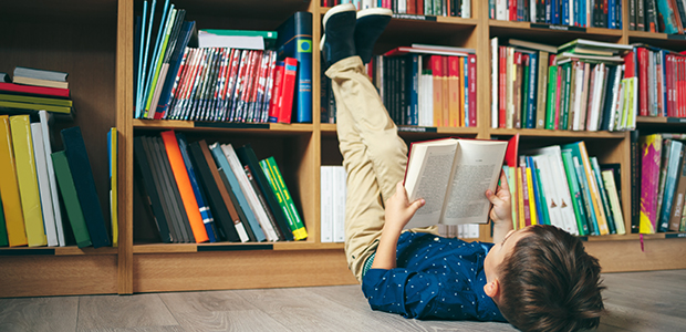 Pojke ligger på golvet och läser i ett bibliotek.  
