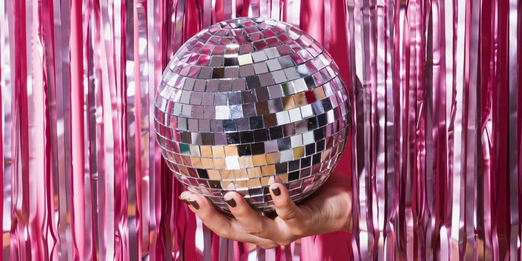 En hand lyfter ut en diskokula genom en rosa glittergardin.