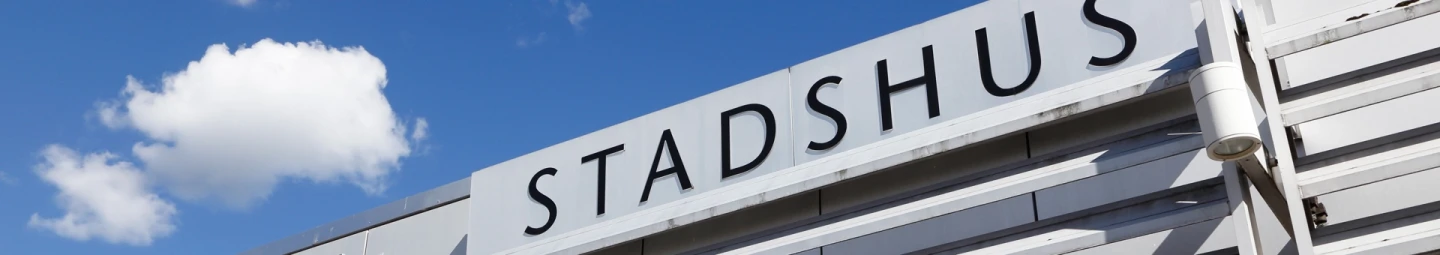 En närbild på en skylt på ett stadshus med himlen i bakgrunden.