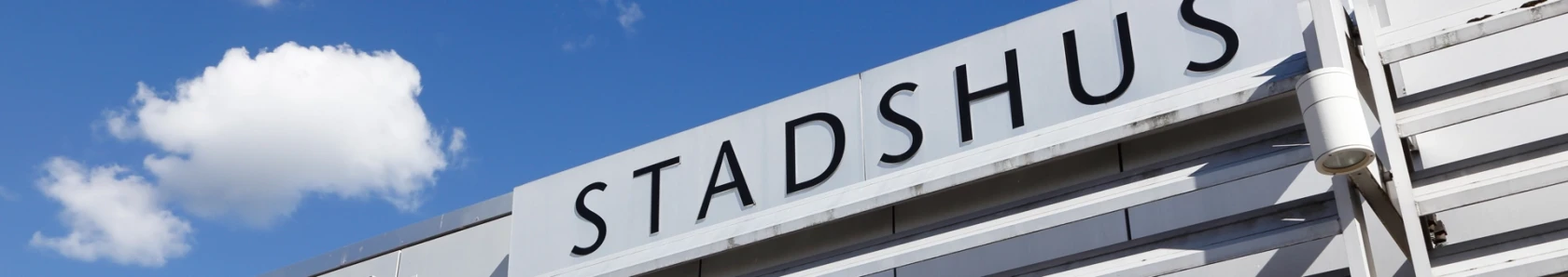 En närbild på en skylt på ett stadshus med himlen i bakgrunden.