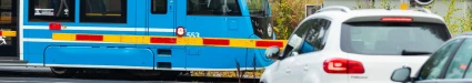Ett blått tåg som färdas bakom vägbommar och trafikljus.