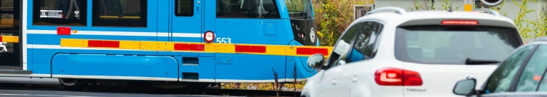 Ett blått tåg som färdas bakom vägbommar och trafikljus.