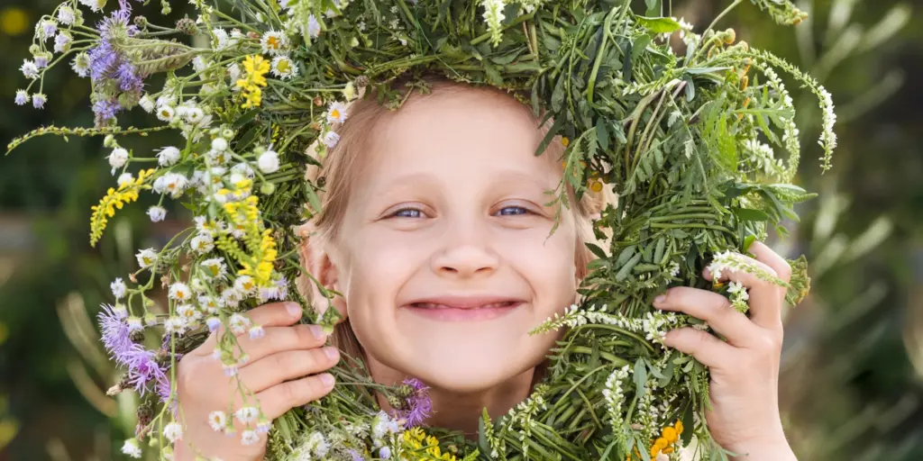Ett glatt barn tittar fram genom en blomsterkrans och ler stort.
