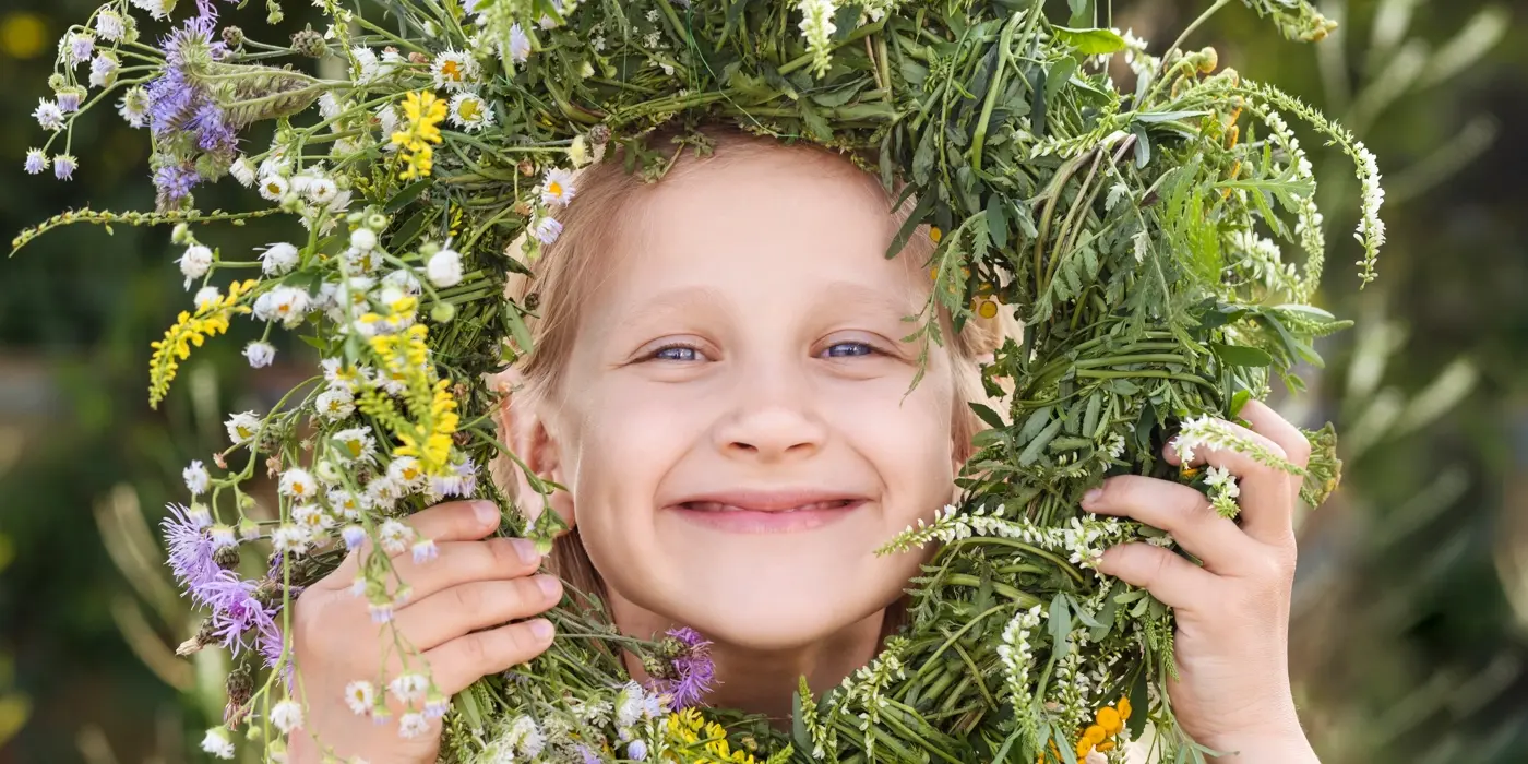 Ett glatt barn tittar fram genom en blomsterkrans och ler stort.
