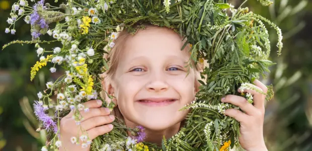 Ett glatt barn tittar fram genom en blomsterkrans och ler stort.