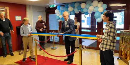 Man klipper band på Lillåkers skola med personer som tittar på. I bakgrunden sitter ballonger och på golvet ligger en röd matta