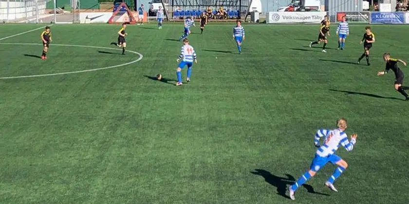 Fotbollsspelare i blåvita kläder springer på grön fotbollsplan