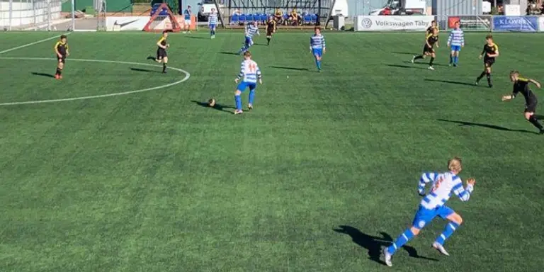 Fotbollsspelare i blåvita kläder springer på grön fotbollsplan