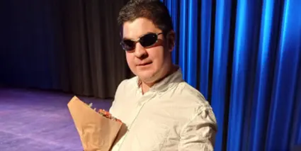 Funkisfestivalens vinnare Joel Brar står på en scen med en vit skjorta och svarta solglasögon framför ett blått draperi