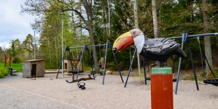 Lekpark med gungställningar och en fågelskupltur.
