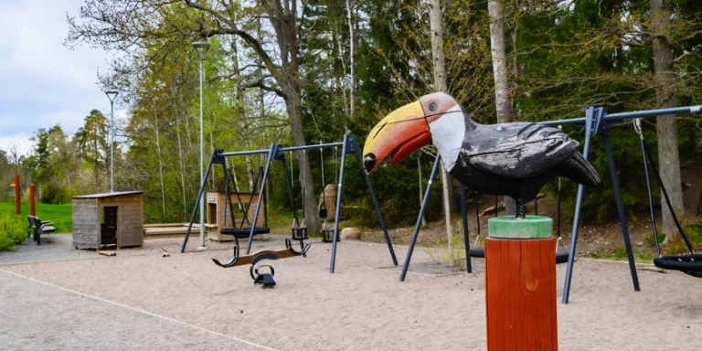 Lekpark med gungställningar och en fågelskupltur.