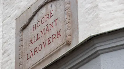 En närbild av en äldre skylt på en byggnad för högre allmänt läroverk.