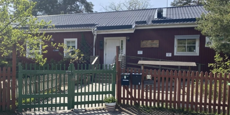 Ett rött hus med en vit dörr och ett grönt staket.