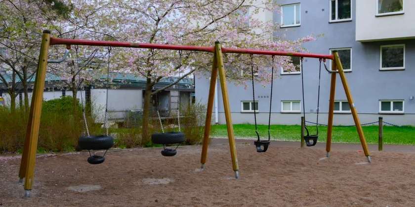 En lekpark med en gungställning bredvid ett flerbostadshus.