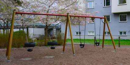En lekpark med en gungställning bredvid ett flerbostadshus.