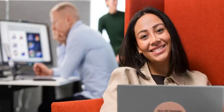 En kvinna sitter i en fåtölj med en bärbar dator på ett kontor.