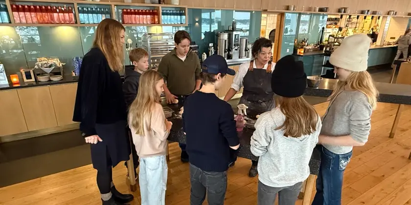 Elever står vid en köksö och får titta på matlagning
