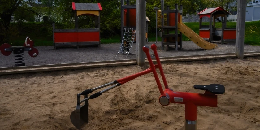 En lekpark med en stor sandlåda med en grävskopa och flera lekställningar.