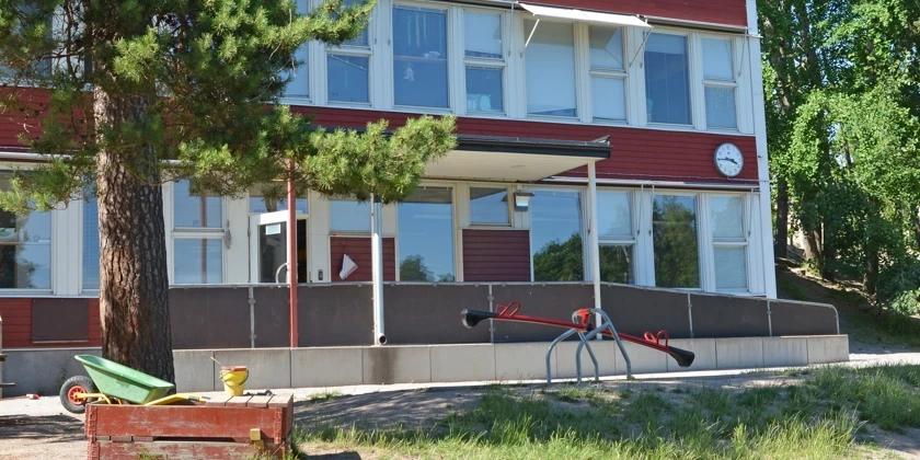 Rudboda förskolas röda, vita fasad med utegård i förgrunden.