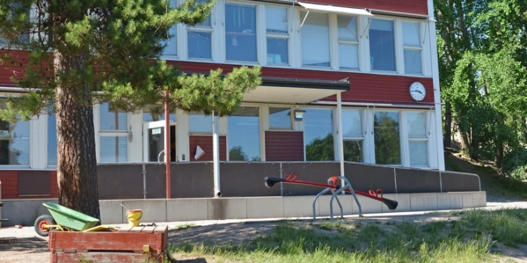 Rudboda förskolas röda, vita fasad med utegård i förgrunden.