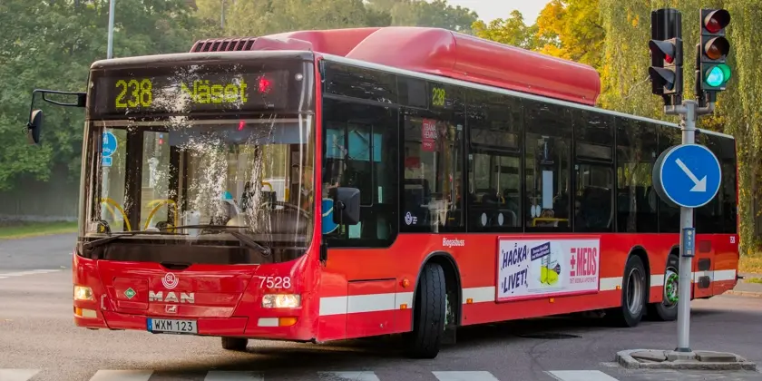 En röd buss svänger i en korsning med trafikljus. 