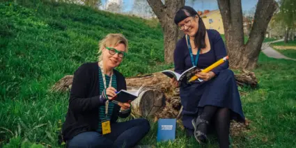 Två kvinnor sitter i gräset med varsin bok i handen