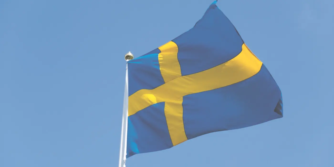 En svensk flagga som vajar mot en klarblå himmel.