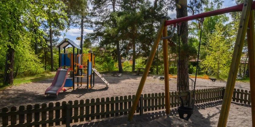 En lekpark med lekställning och babygunga omgiven av träd.