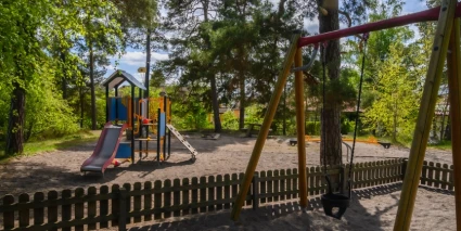En lekpark med lekställning och babygunga omgiven av träd.