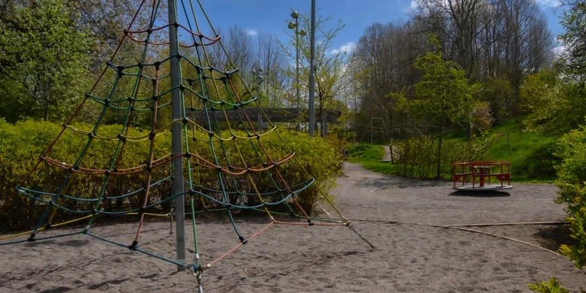 Ett klätternät i en lekpark omgiven av grönska.