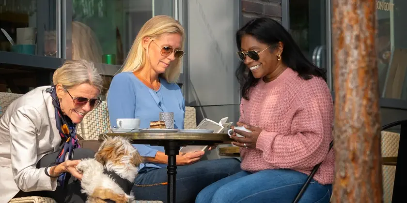 Tre kvinnor sitter vid ett kafébord med en hund.
