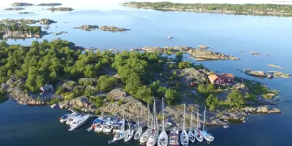 En flygbild över en liten ö med ett rött hus och en båthamn i Stockholms skärgård.