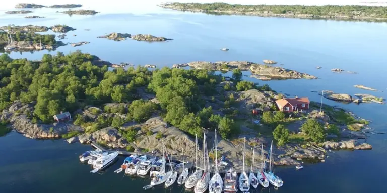 En flygbild över en liten ö med ett rött hus och en båthamn i Stockholms skärgård.