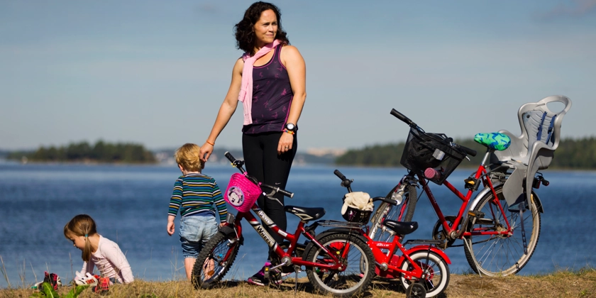 En mamma med sina två små barn har stannat med sina cyklar vid vattnet.