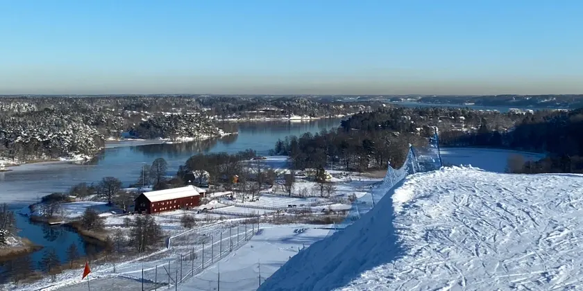 Utsikt över vatten och skog från toppen av en skidbacke.