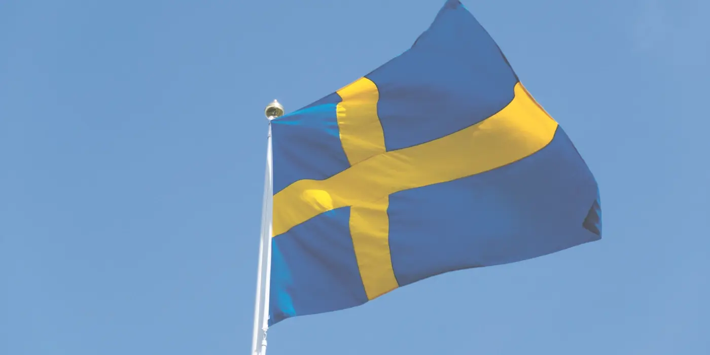 En svensk flagga som vajar mot en klarblå himmel.