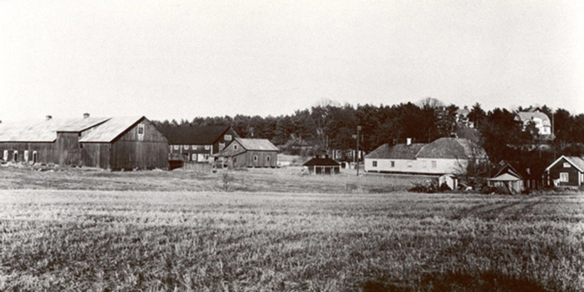 Ett svartvitt foto av en gård med en åker i förgrunden.