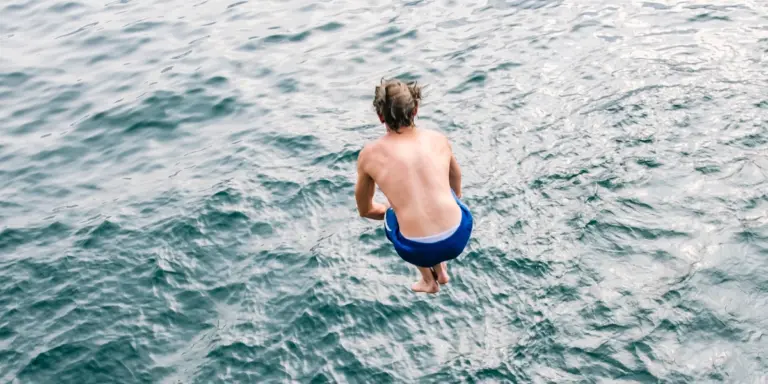 En man hoppar i havet med ryggen mot kameran.